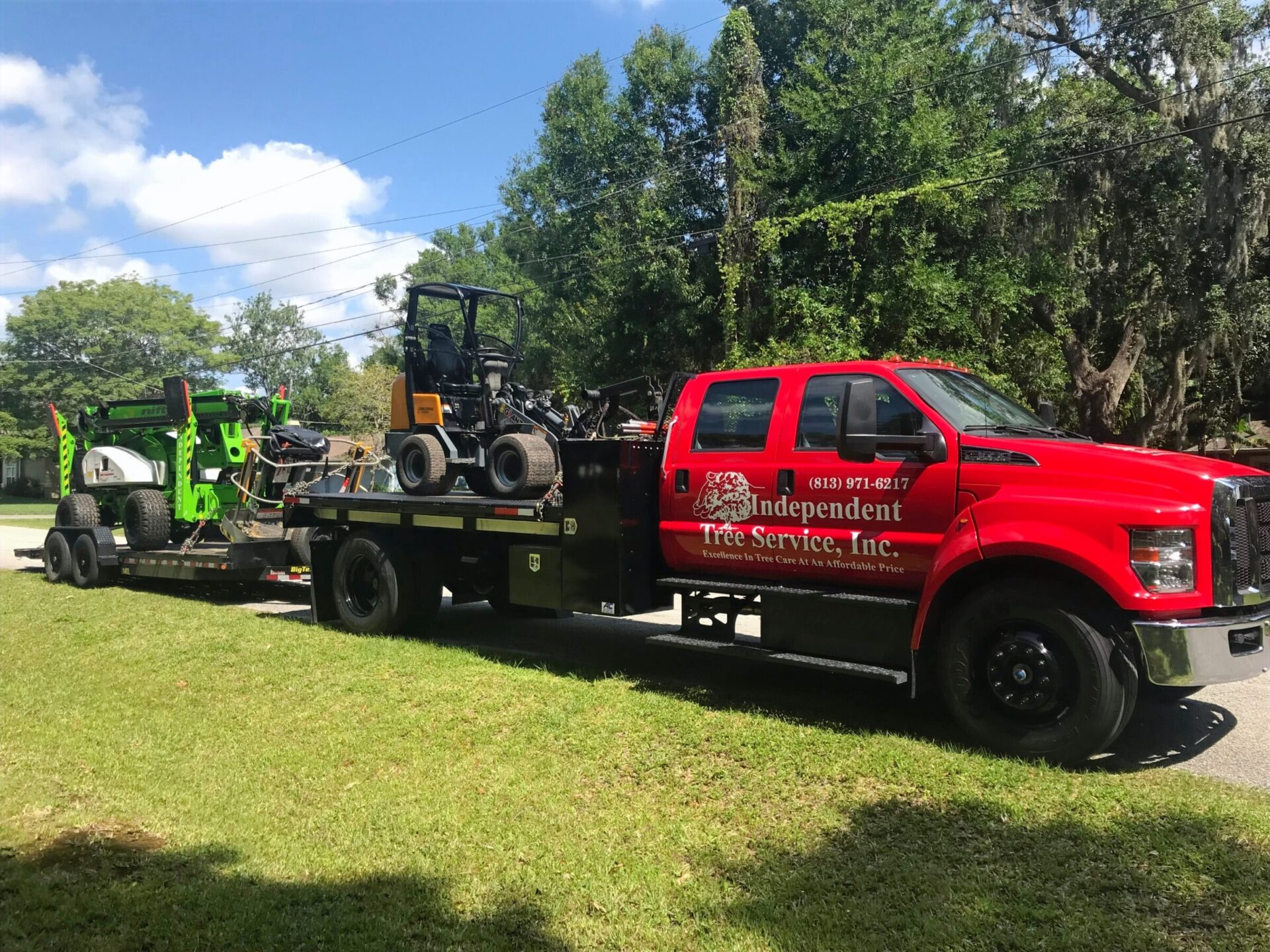 A red truck from Independent Tree Service, Inc. tows tree maintenance equipment on a sunny day, parked on a grassy roadside.